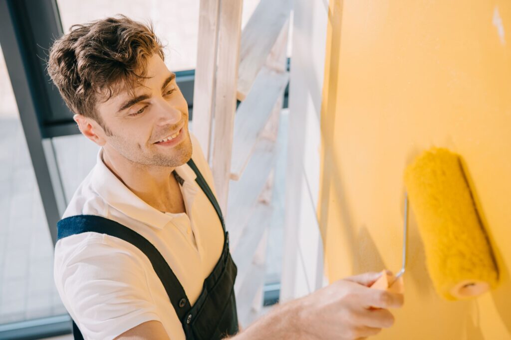 handsome-young-painter-smiling-while-painting-wall-2023-11-27-05-05-35-utc