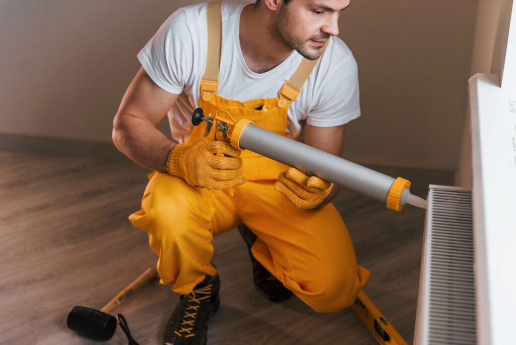 handyman-in-yellow-uniform-works-indoors-with-heat-2023-11-27-05-30-32-utc