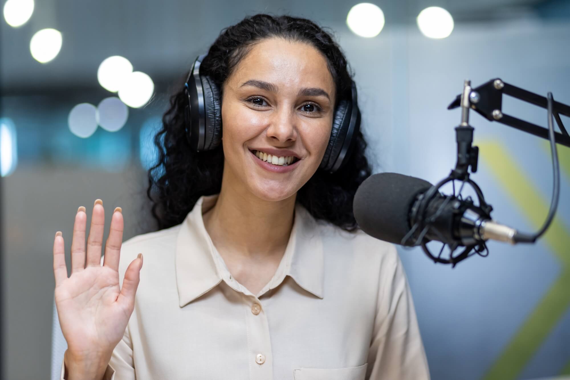 smiling-woman-with-headphones-waving-during-podcas-2024-08-02-14-54-52-utc